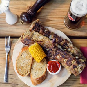 Ripperlan mit Mais und Knoblauchbrot am Tisch mit einem dunklen Hausbier