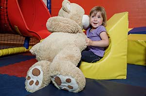 Mädchen spielt mit großen Teddy in einer Spielecke die ausgepolstert ist.